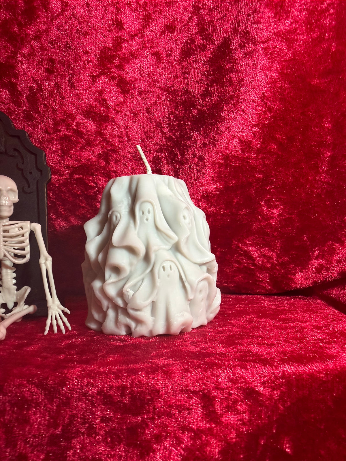 White sculpted ghost-stack pillar candle on a red fabric backdrop.